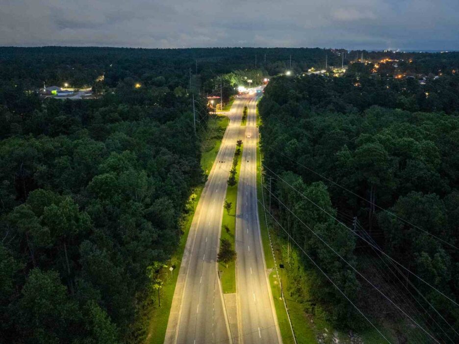 Aerial view of solar-powered streetlights illuminating a Georgia highway through a forested corridor, providing safe, off-grid lighting at night.