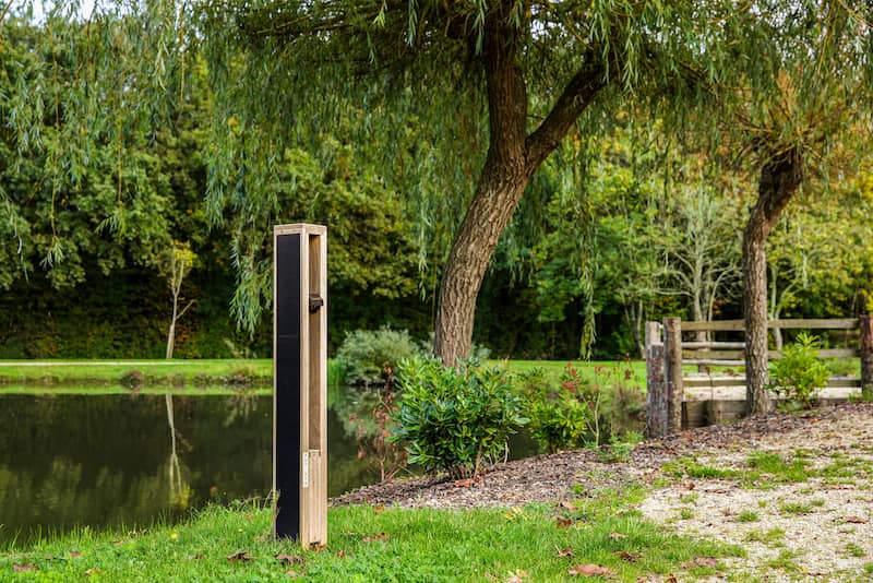 Nowatt solar bollard light installed beside a pond and pathway in a landscaped park setting.