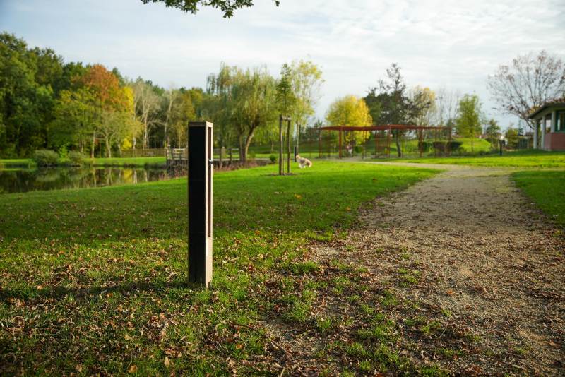 Nowatt solar bollard installed beside a park pathway near a pond, providing sustainable off-grid lighting in a landscaped setting.