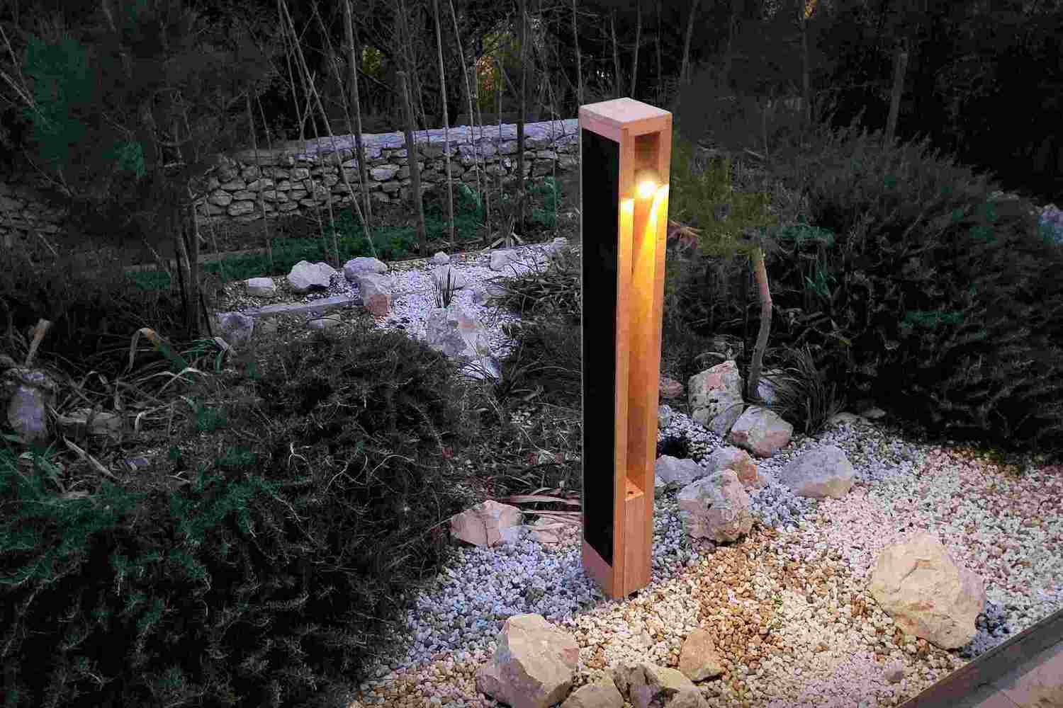 Modern solar bollard light illuminating a landscaped garden pathway, blending into natural surroundings with minimalist design.