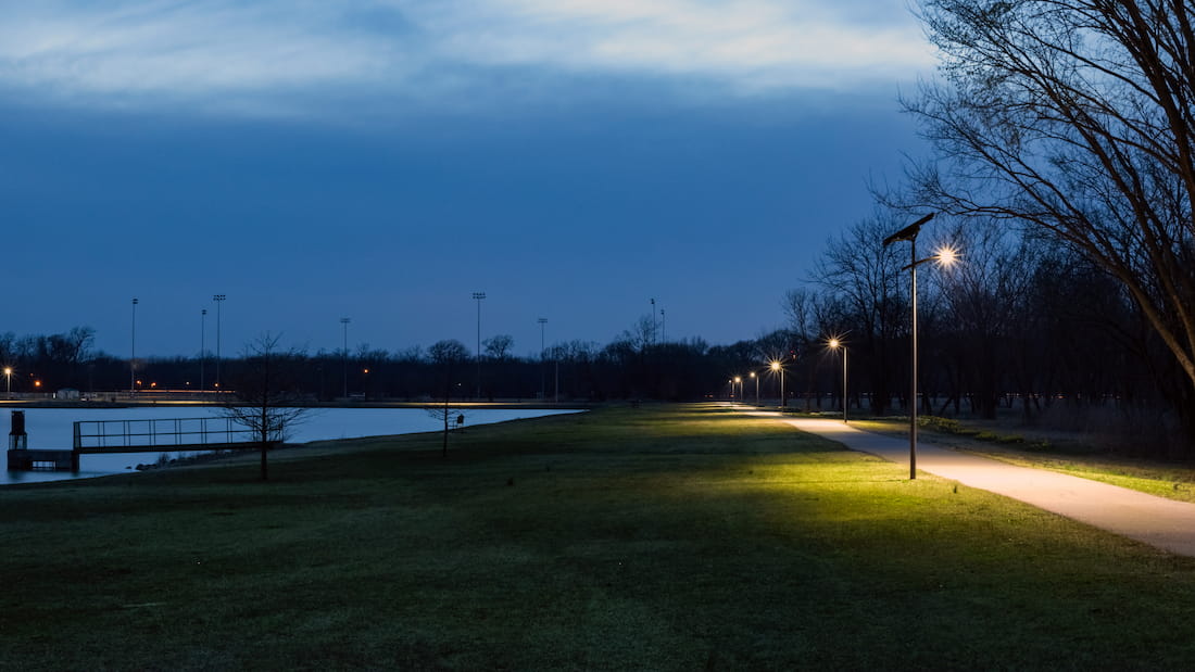 Solar-powered lights illuminating a walking trail around a lake, providing energy-efficient lighting for outdoor enthusiasts.
