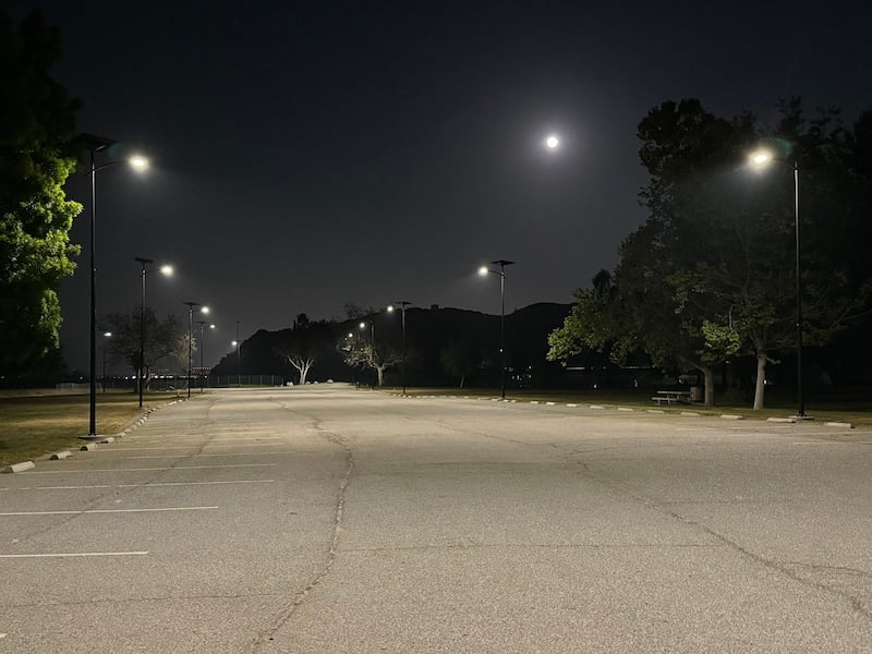 Solar-powered Fonroche streetlights providing uniform illumination across a public parking lot at night under a full moon