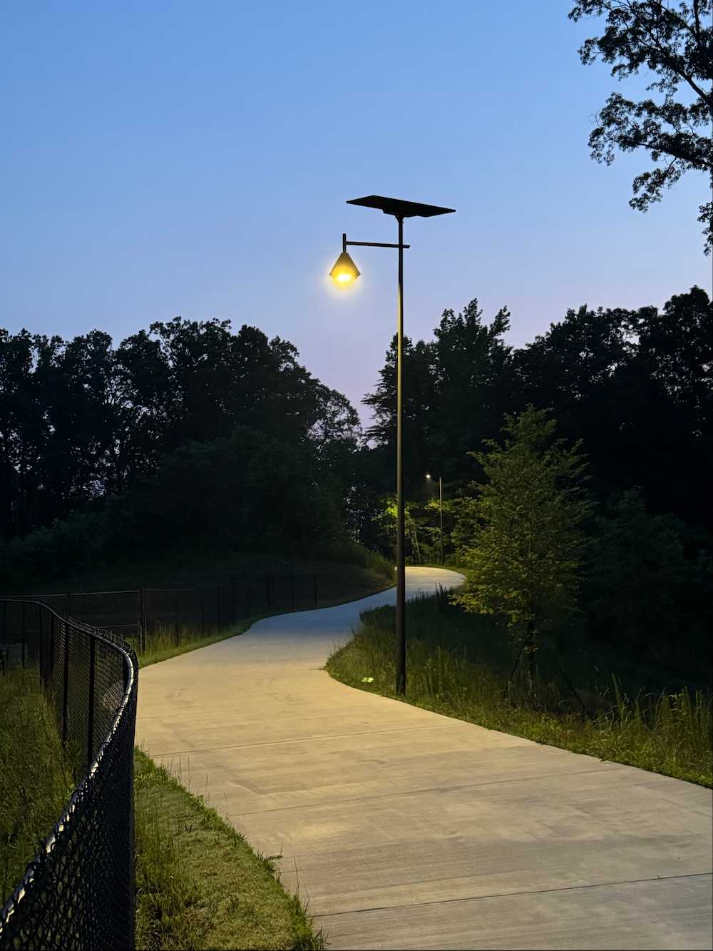 Solar-powered streetlight illuminating a winding pedestrian path at dusk, surrounded by trees and natural greenery in Georgia 